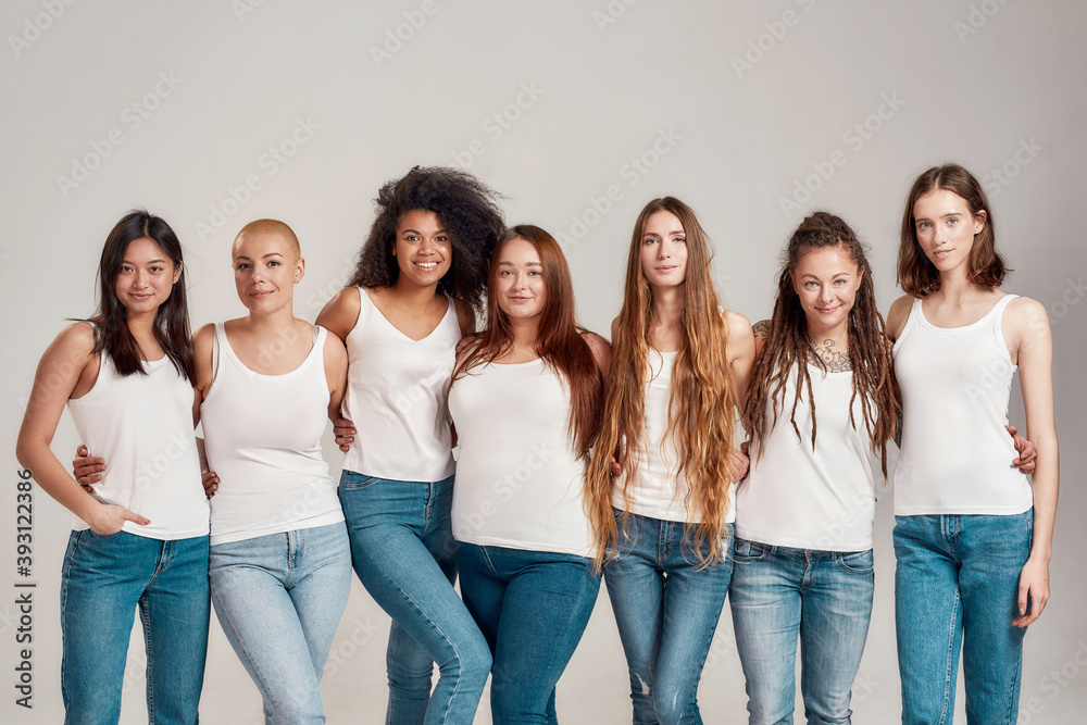 Group of beautiful diverse young women wearing white shirt and denim jeans