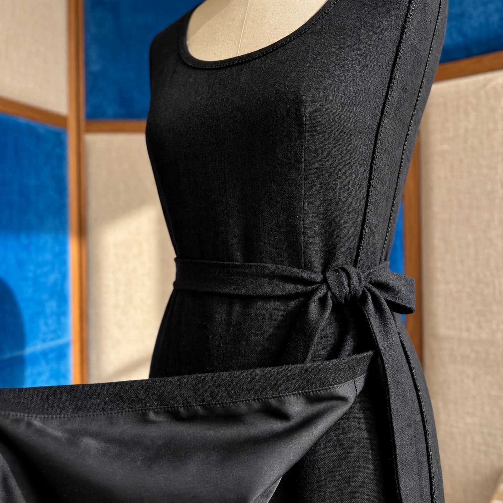 A black midi dress displays its waist tie, side seam, and lined hem.