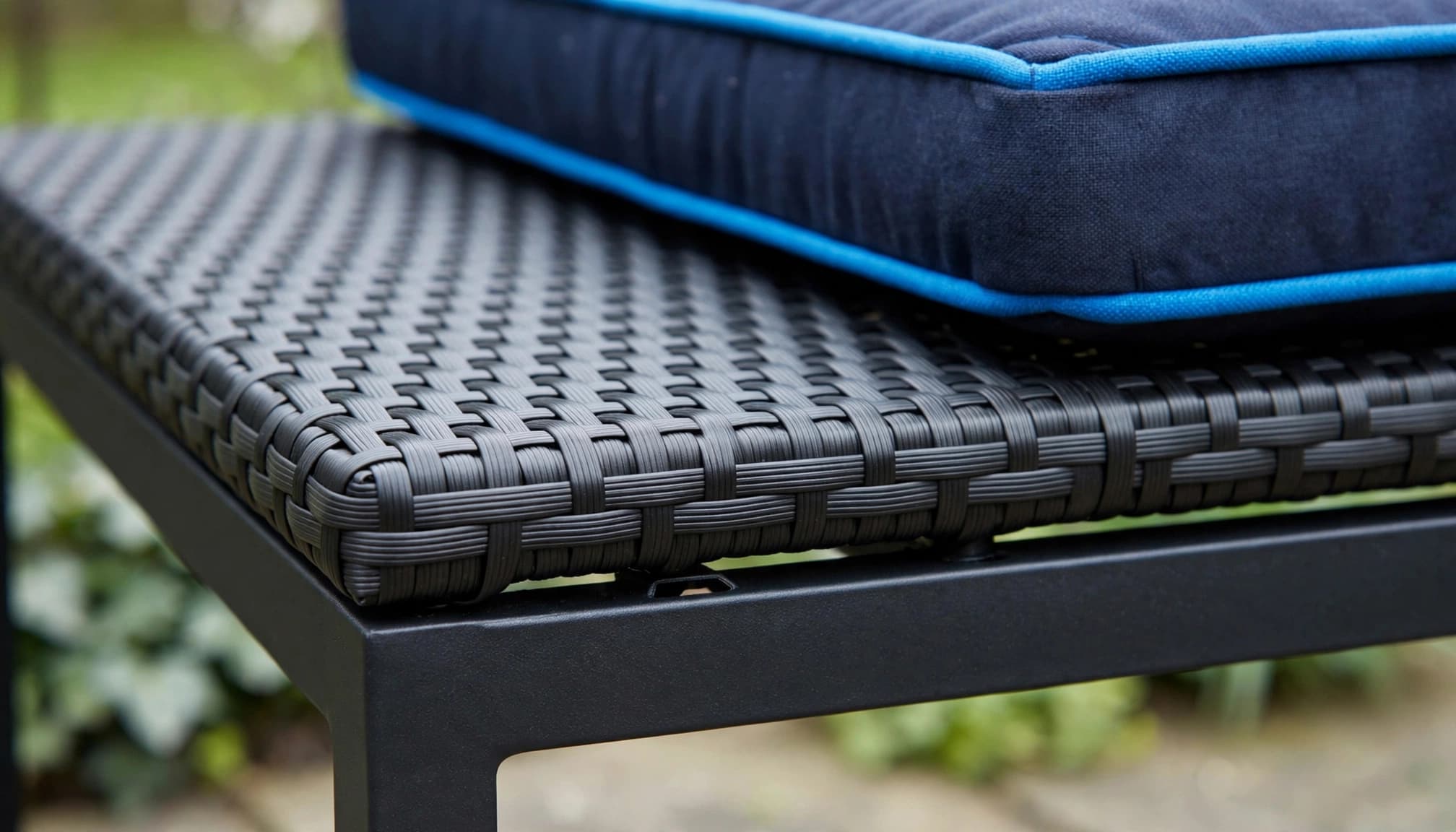Close-up of black rattan furniture with a cushion, metal frame, and drainage gap.