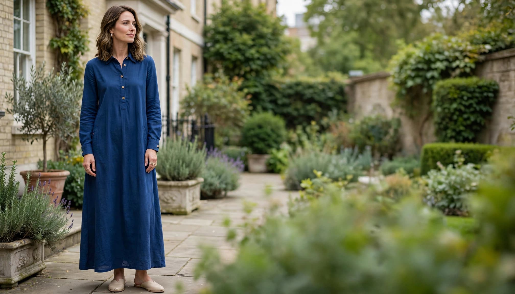 Woman in a blue cotton maxi dress beside greenery in a townhouse garden.