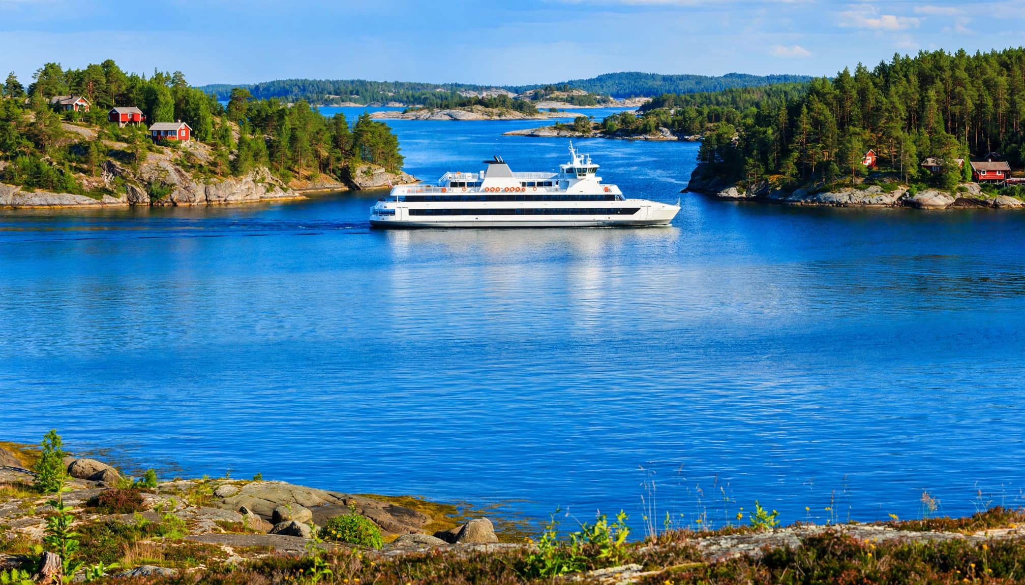 A passenger ferry crossing calm Baltic water between forested Finnish islands.