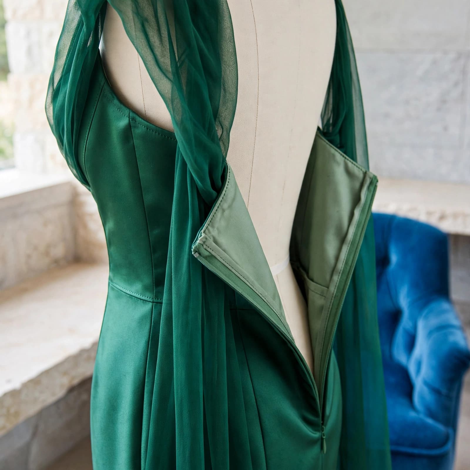 A green gown on a dress form beside a blue chair, showing its seams and fabric drape.