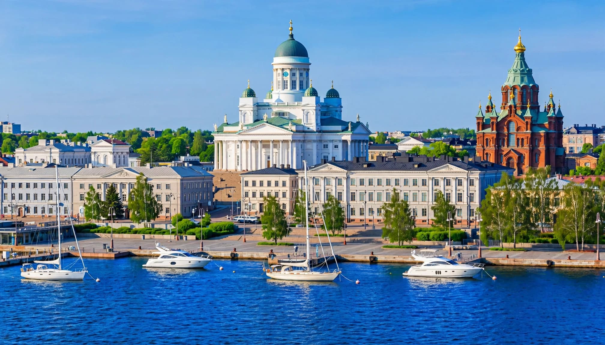 Historic Helsinki buildings and boats line a calm waterfront on a bright summer morning.