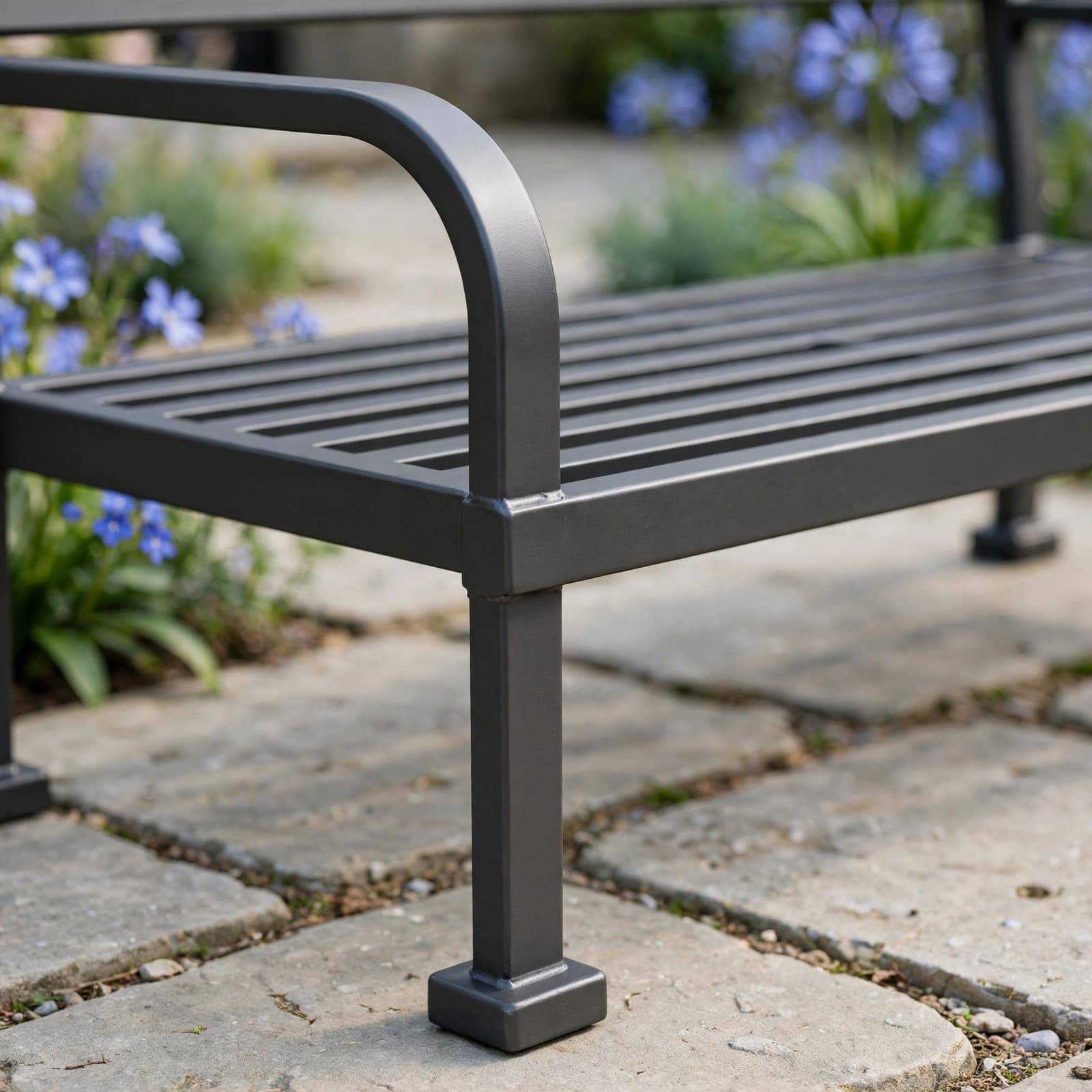 Metal Garden Bench Buying Guide: Comfort, Rust and Value 2 A metal garden bench with a smooth armrest and slatted seat on stone paving.