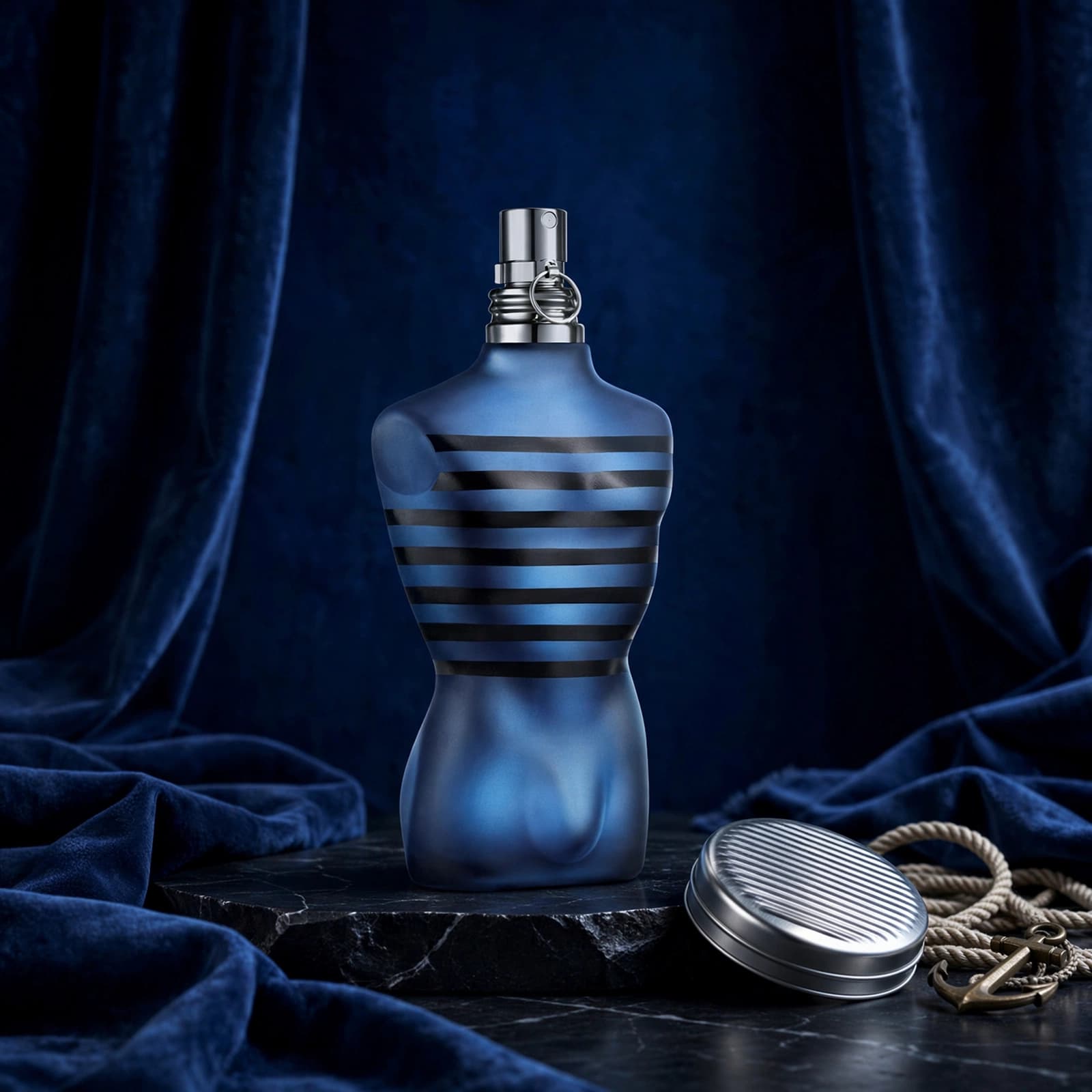 Jean Paul Gaultier Ultra Male Review: Bold, Sweet and Built for Evenings 1 A navy torso-shaped fragrance bottle beside a metallic tin on blue velvet.