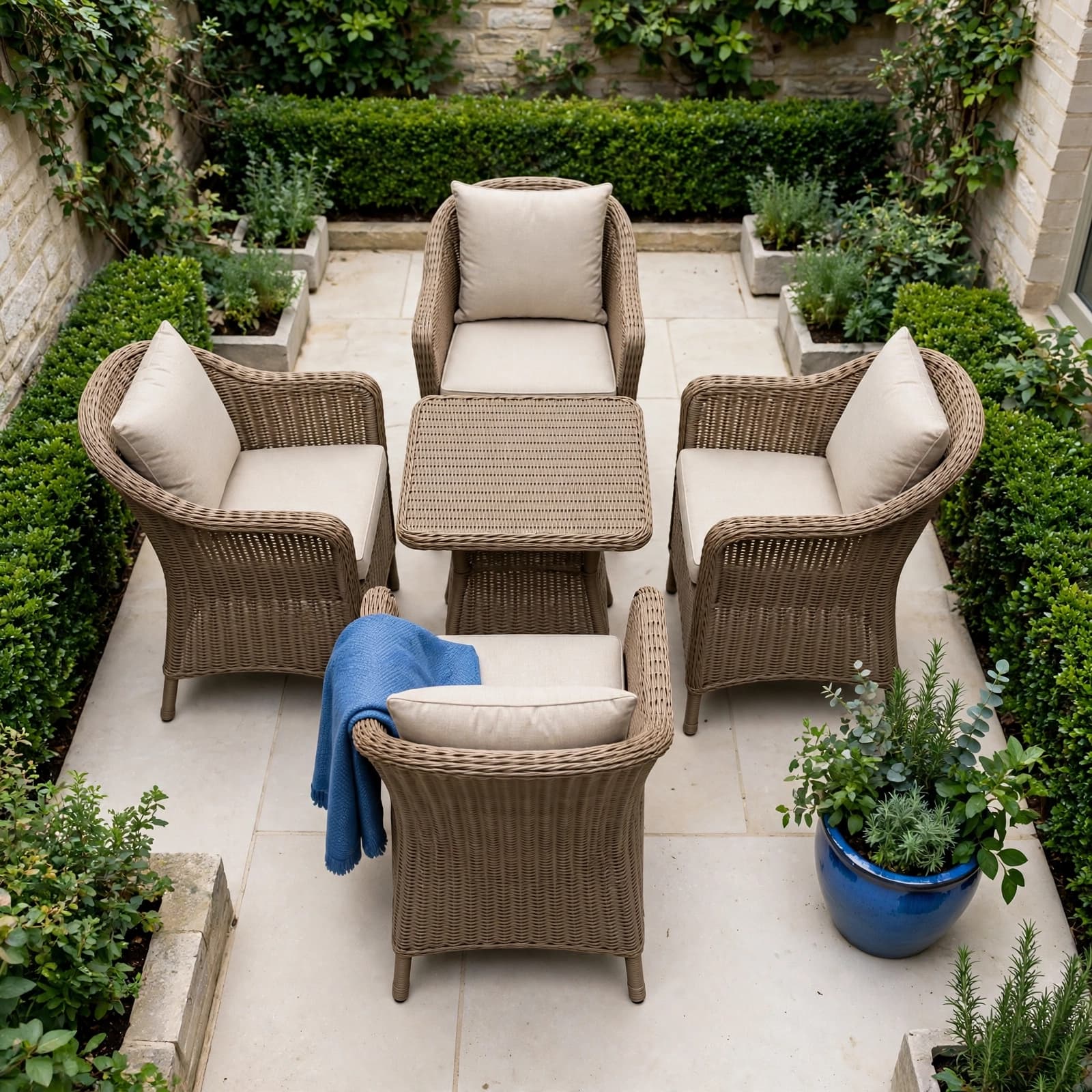 Four cushioned rattan chairs surround a compact table on a stone courtyard patio.
