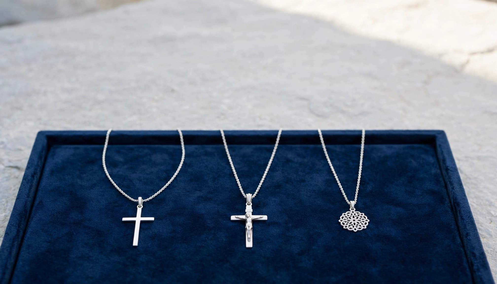 Cross Necklace Buying Guide: Style, Quality and Value 1 Three silver necklaces, including a cross and crucifix, on blue velvet.